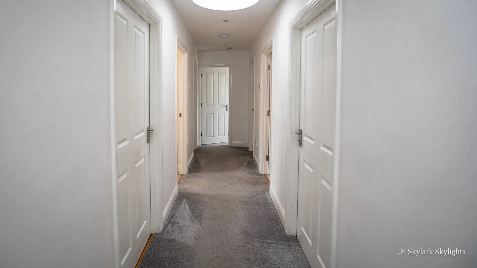 Carpeted hallway with white doors and a sun tunnel in the ceiling