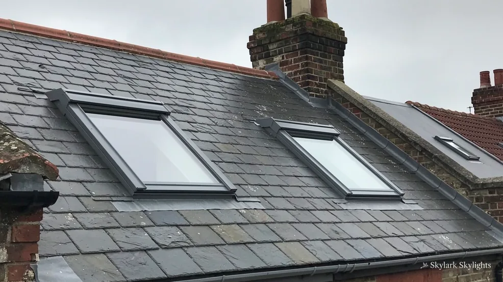 Two roof windows in a slate roof beside a chimney