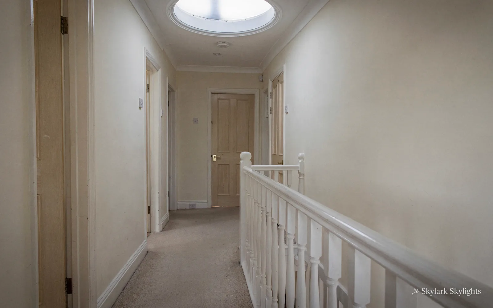 Upstairs landing with a white banister and a sun tunnel above