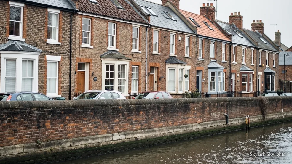 Row of brick terraced houses facing water, roofs lined with chimneys