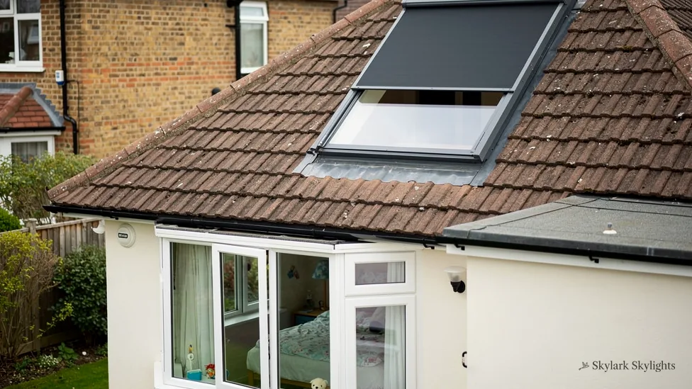 Roof window in a brown tiled roof above a bungalow wall