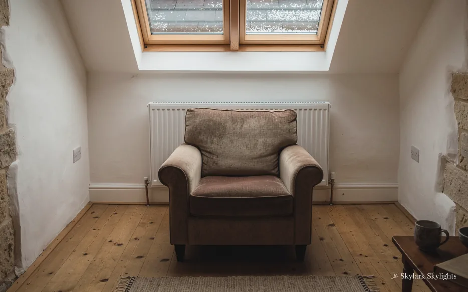 Armchair below roof windows on bare floorboards