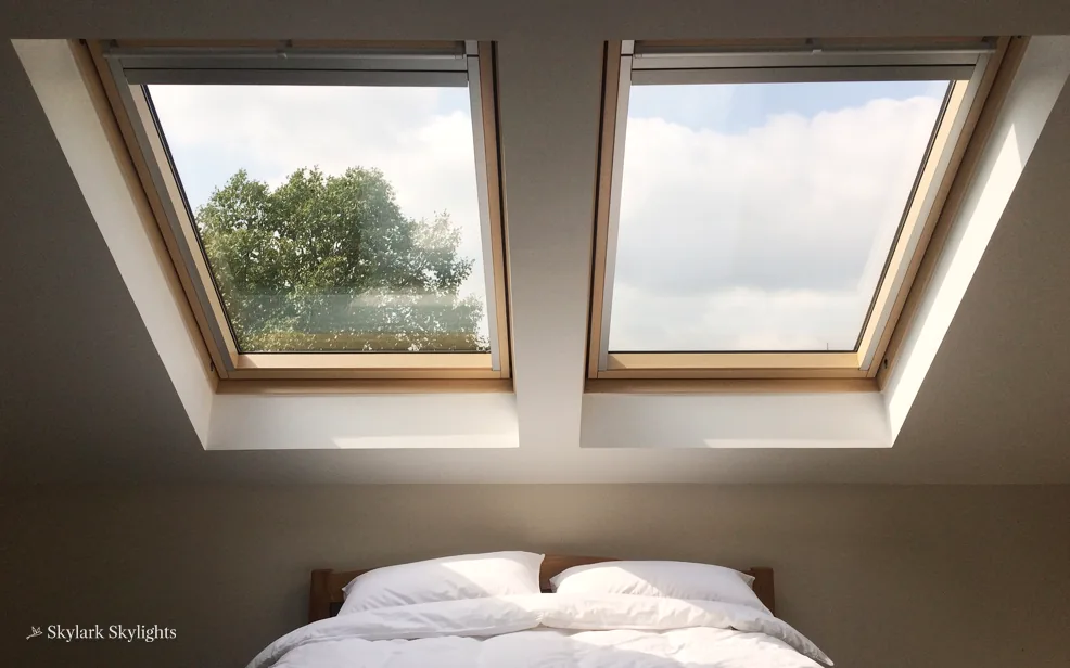 Bed below two roof windows with trees outside