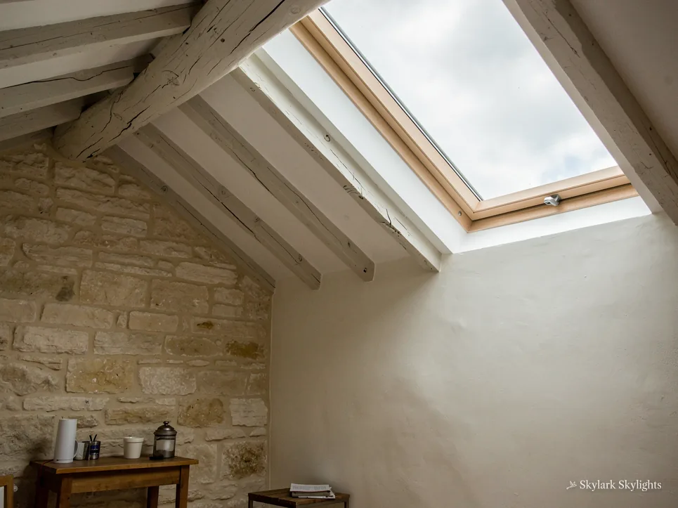 Stone-walled loft room under exposed beams with a roof window