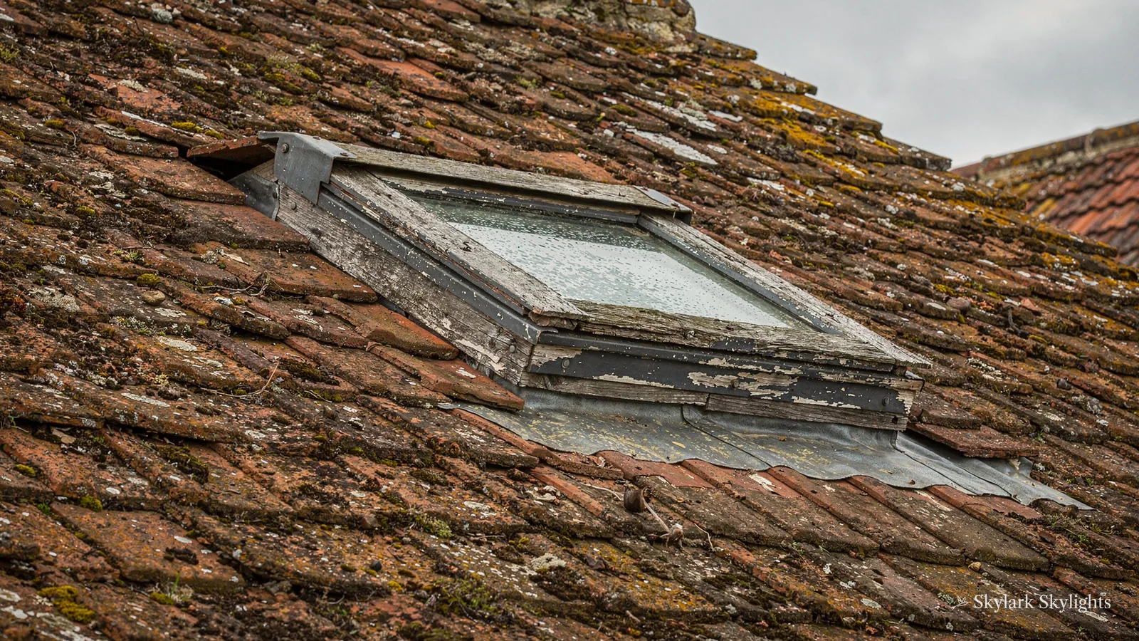 Roof window with weathered flashing in an old clay-tiled roof