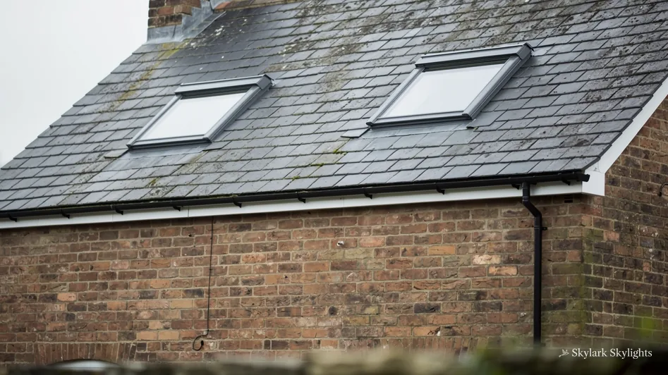 Two roof windows in a slate roof above a brick wall