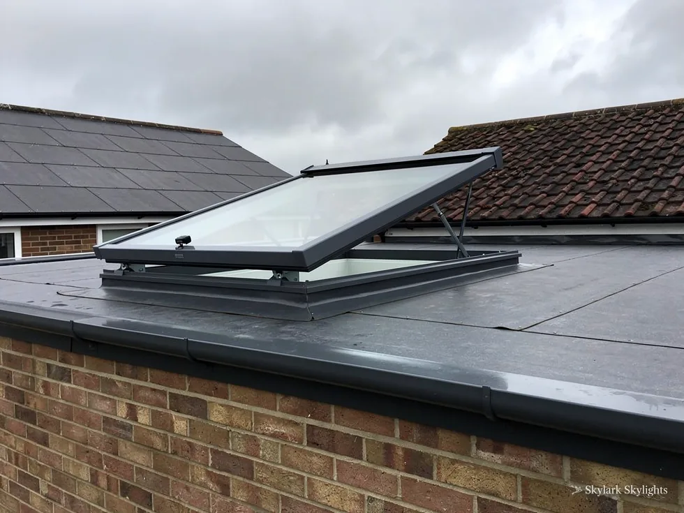 Opening rooflight on a flat roof above a brick wall, sash raised