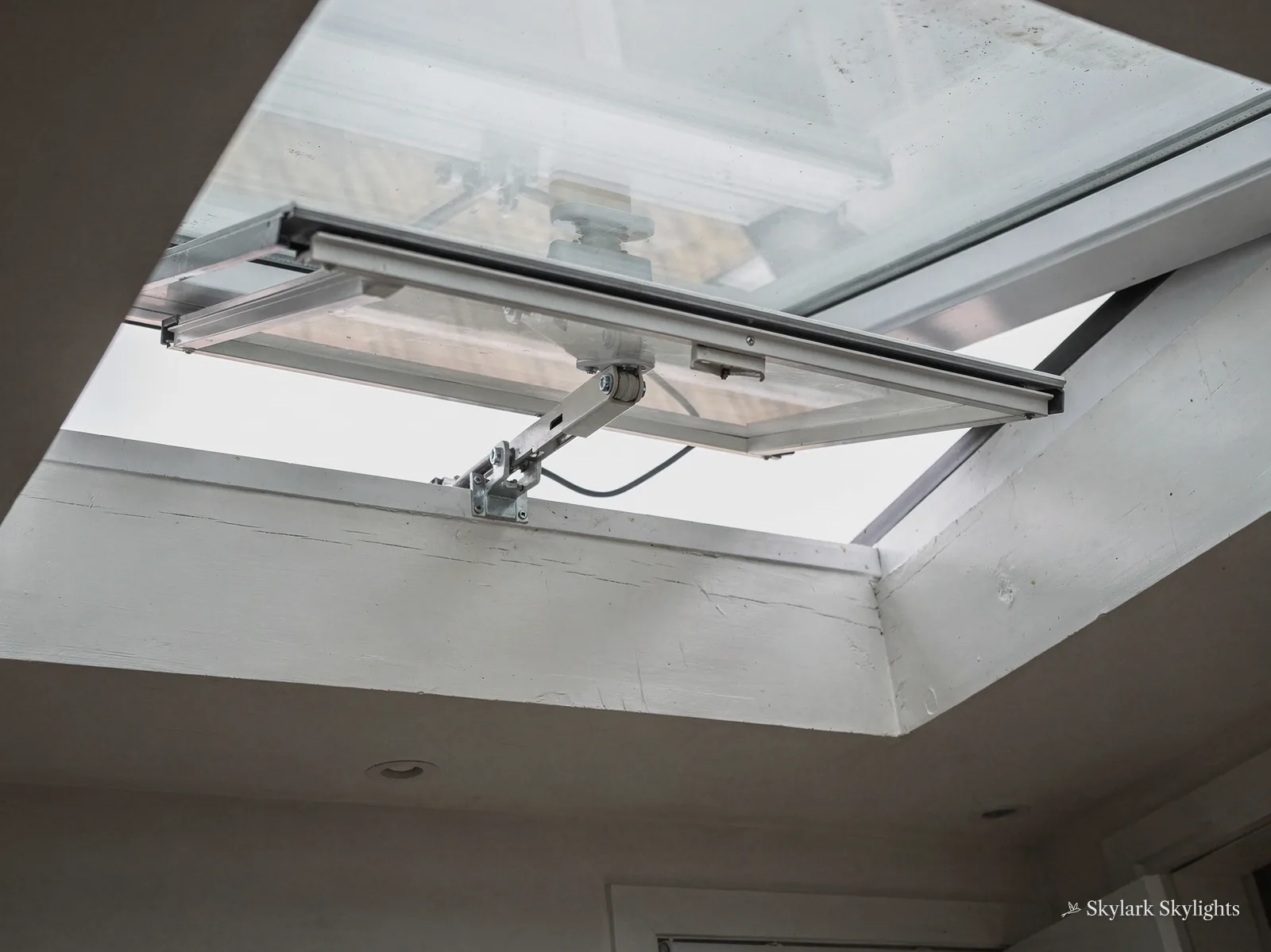Looking up at an open rooflight on its motor arm in a white room