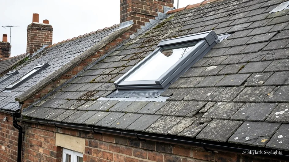 Roof window in a slate roof with brick chimneys beyond
