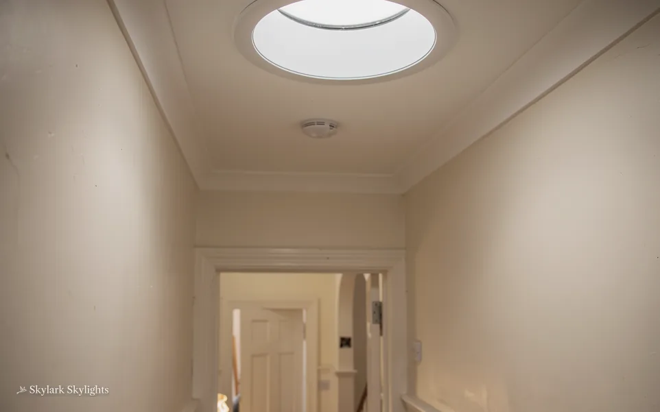 Hallway towards a door, lit by a round sun tunnel