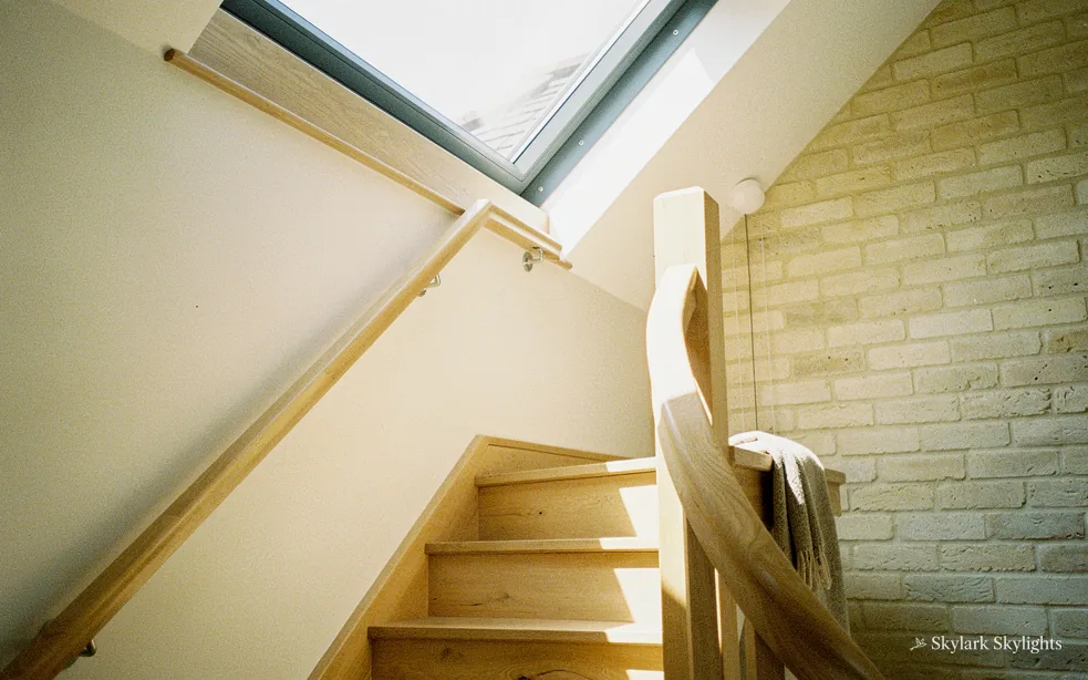Stairs climbing past a stone wall towards a roof window
