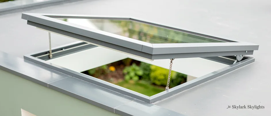 Opening rooflight tilted up on a pale flat roof, plants visible below