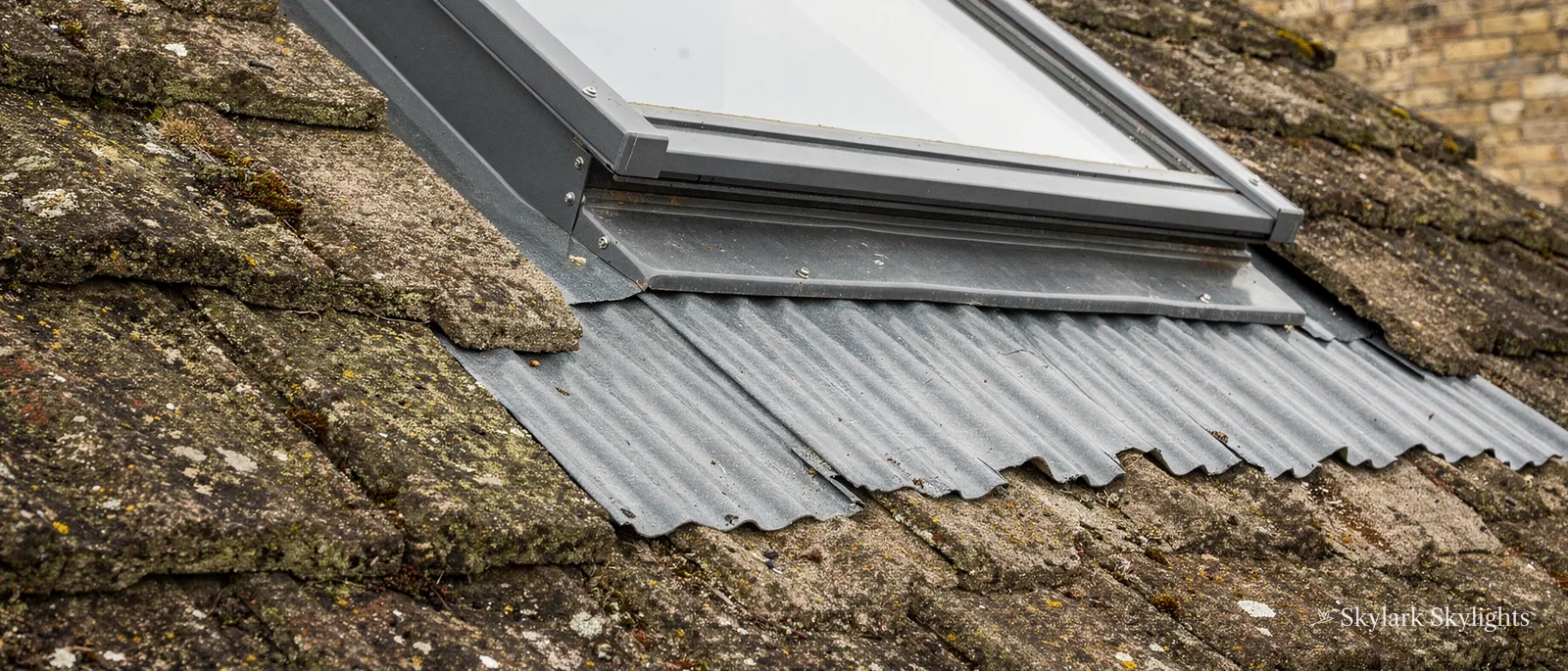 Old roof window with grey flashing in a mossy tiled roof