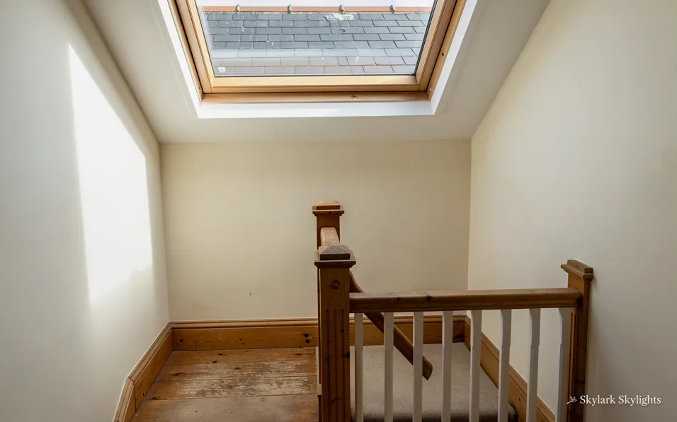 Stair landing with a wooden handrail under a roof window