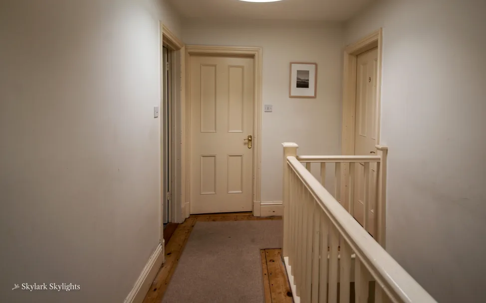 Narrow landing with a white banister and doors off