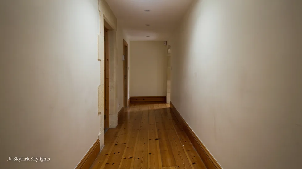 Long narrow corridor with wooden floorboards and plain white walls
