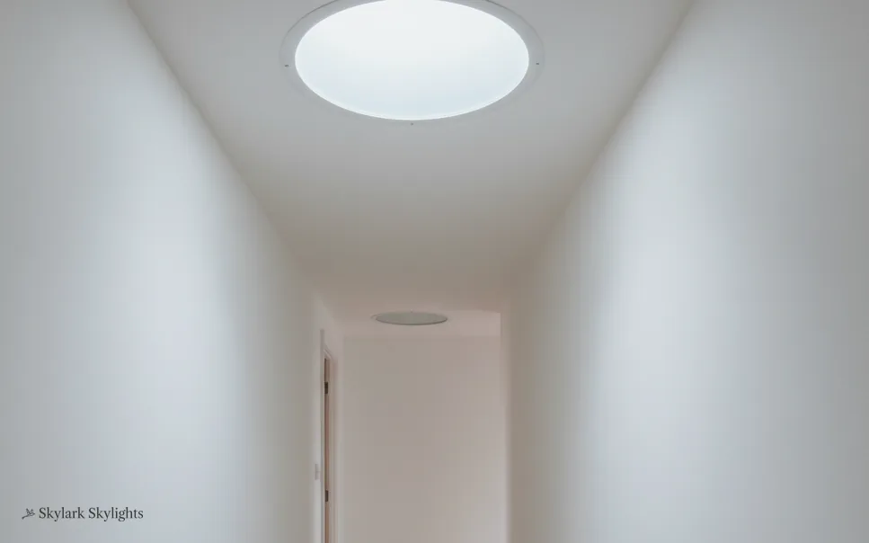 Narrow white room lit by a round sun tunnel