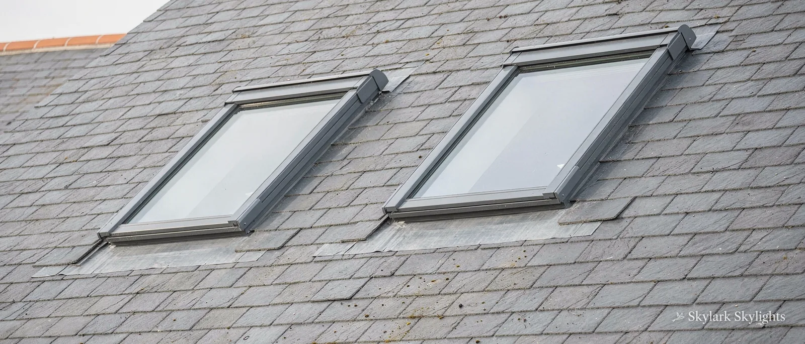 Two roof windows side by side in a grey slate roof