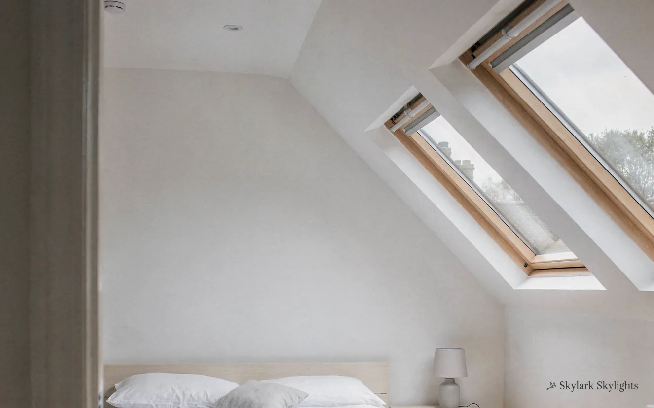 Bed tucked under a pair of roof windows in a white loft